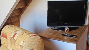 Un televisor sobre un soporte de madera con un control remoto a un lado, un sofá estampado y un techo inclinado.