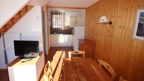 Una cocina compacta con comedor, paredes de madera y un televisor sobre un mueble.