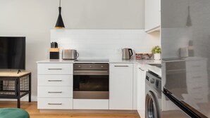 Eine moderne Küche mit weißen Schränken, einem Edelstahlbackofen, einer Waschmaschine und einem Flachbildfernseher.