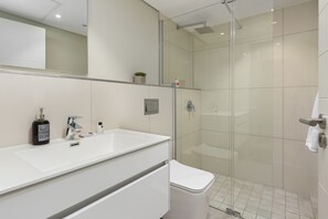 Un baño moderno con un lavamanos blanco, un espejo, una ducha de vidrio y un inodoro.