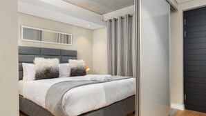 Ein modernes Schlafzimmer mit einem grau gepolsterten Bett, weißer Bettwäsche und einem grauen Kopfteil.