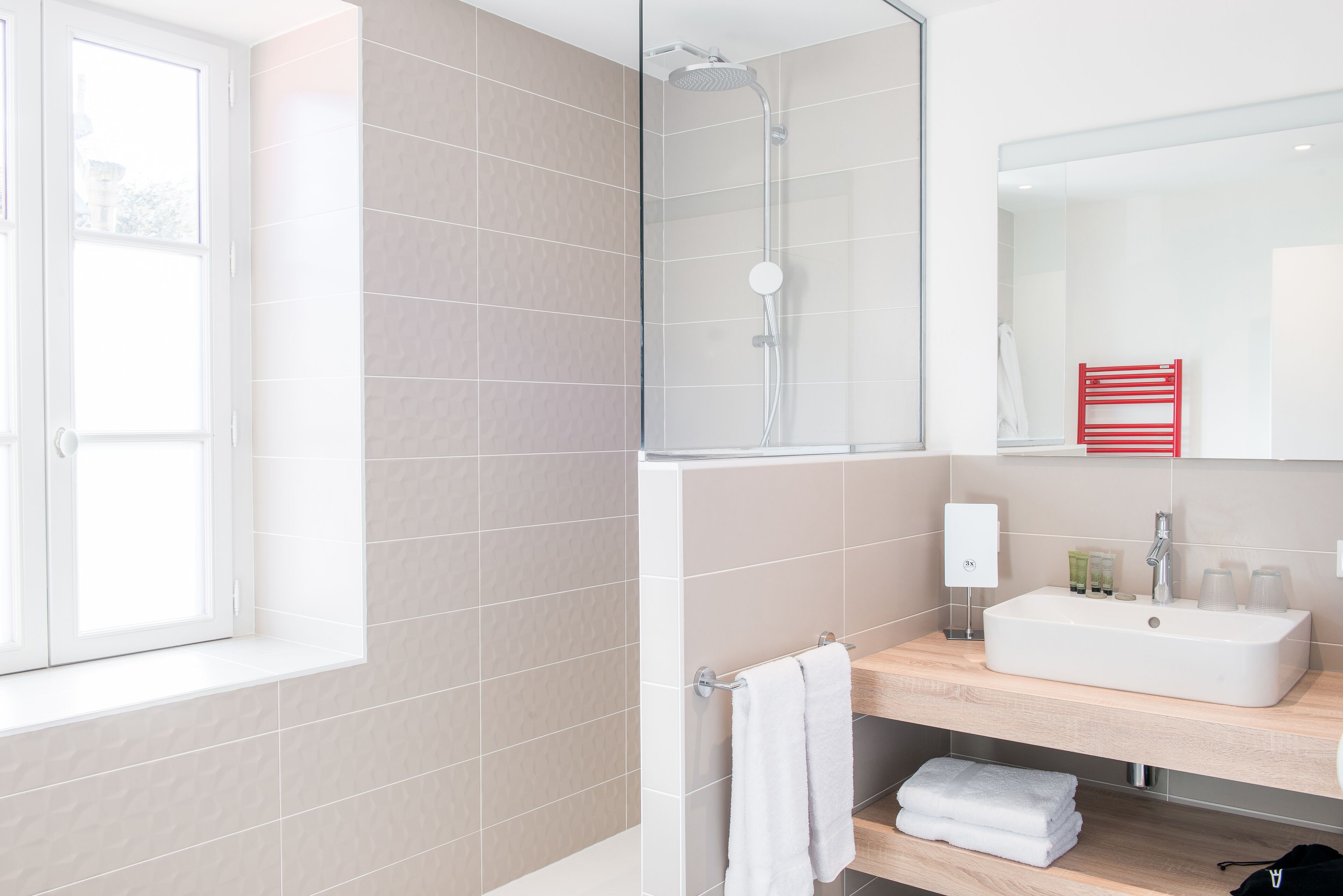 Een moderne badkamer met een douchecabine van glas, een witte wastafel en een spiegel erboven.
