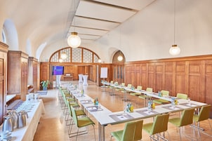 Un salón de conferencias con mesas largas, sillas verdes y paneles de madera.