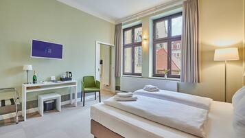 A hotel room with a bed, a desk, a chair, a TV, and a window with a view of buildings.