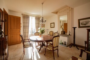 A dining room with a round wooden table, six striped chairs, a chandelier, and a fireplace with a mirror above it. - Charming house village - heated private pool & outside ktichen (Mézin)