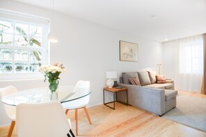 Relax in this stylish living room with a glass dining table, comfortable sofa, and large window offering a serene view of the surrounding trees.