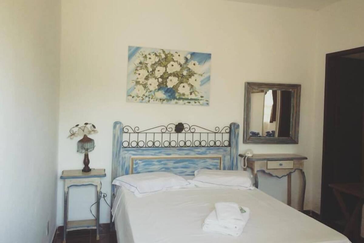 A bedroom with a bed, a bedside table, a nightstand, a painting, and a mirror.