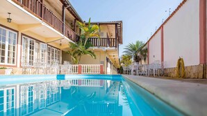 Una piscina con superficie de agua azul cristalina, rodeada por un edificio con balcones y mobiliario exterior.