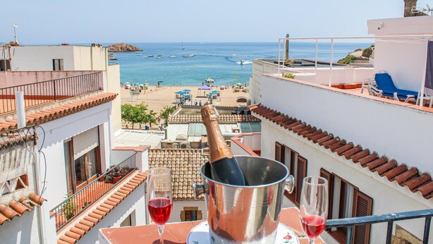 Een balkon met uitzicht op een strand, een metalen emmer en twee glazen rode wijn.