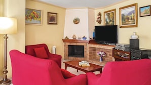Een woonkamer met rode banken, een open haard, een flatscreen televisie en diverse ingelijste foto's aan de muur.