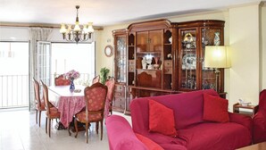 Een woonkamer met een rode bank, een eettafel met stoelen, een kroonluchter en een houten kast met glazen deuren.