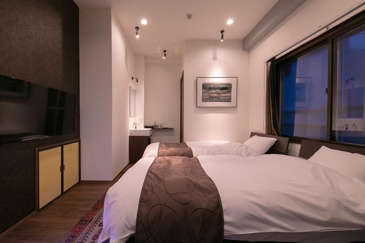 Een moderne hotelkamer met twee bedden, een flatscreen televisie, een schilderij en een raam met uitzicht.