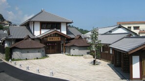 A traditional Japanese building with a tiled roof and wooden structure, a central entrance with a wooden door, and a paved courtyard.