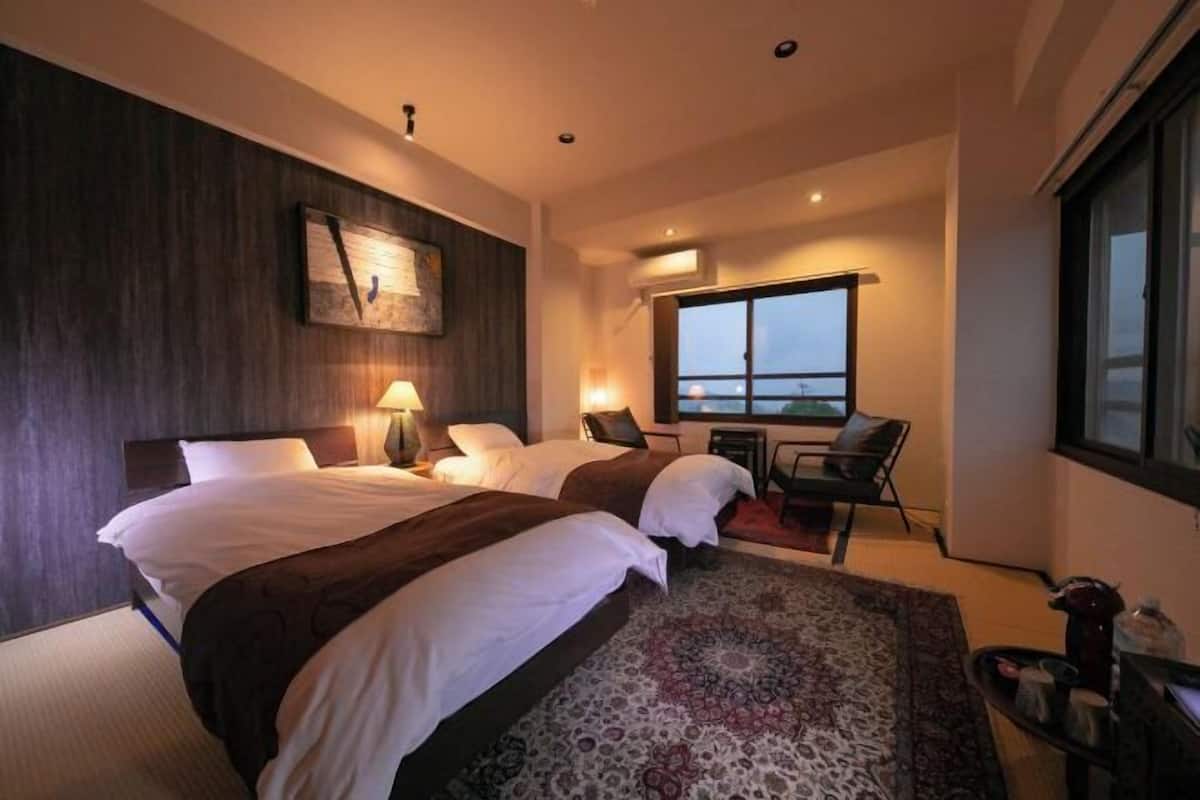 Hotellihuone, jossa on kaksi sänkyä, suuri ikkuna, työpöytä ja näkymä kaupunkiin.