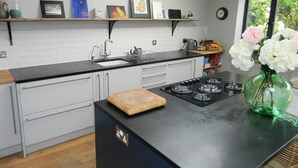 A modern kitchen with a black countertop, white cabinets, a built-in stove, and a window with a view of greenery. - Stunning Period Townhouse (Frome)