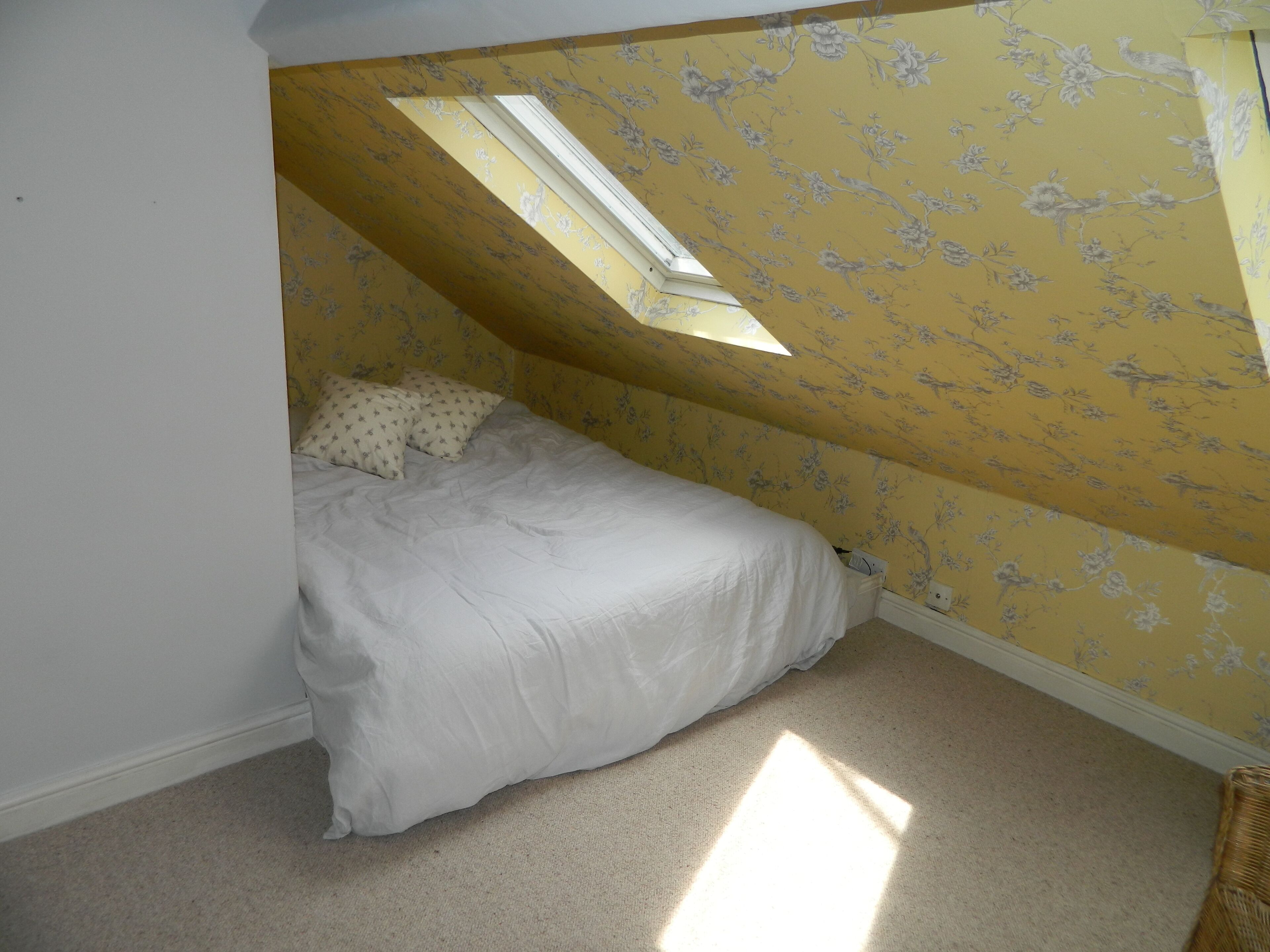 A bedroom with a sloped ceiling, floral wallpaper, a bed with white bedding, and a skylight.
