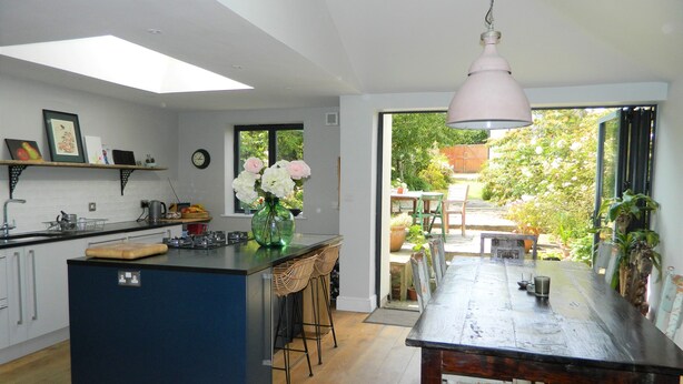 A modern kitchen with a central island, wooden flooring, and a dining area with a view of the garden. - Stunning Period Townhouse (Frome)