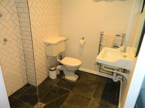 Kylpyhuone, jossa on wc, pesuallas ja laatoitettu lattia.