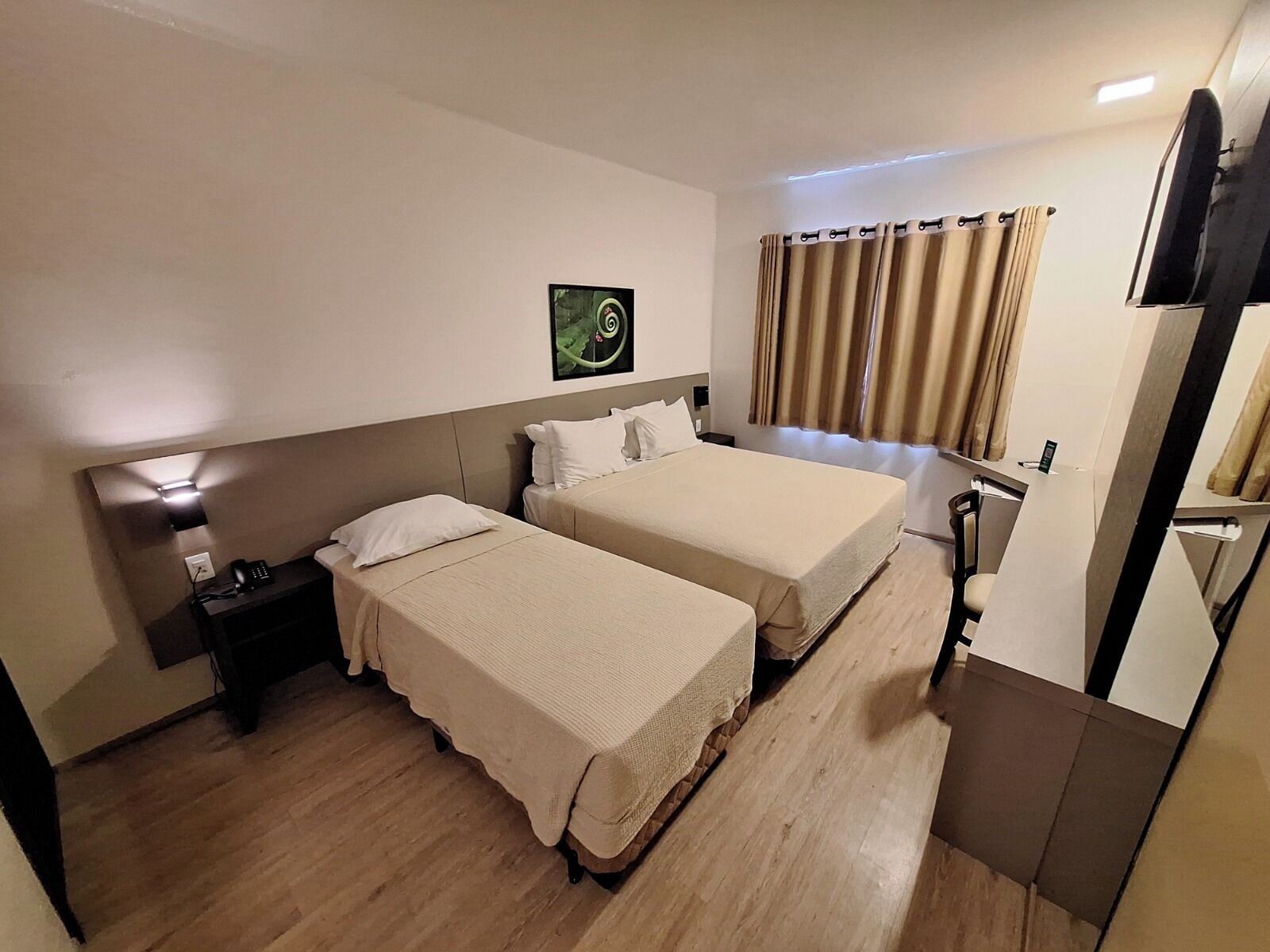 A hotel room with two beds, a desk, a chair, a TV, and a window with curtains.