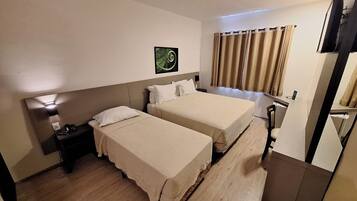 Habitación de hotel con dos camas, un escritorio, una silla, un televisor y una ventana con cortinas.