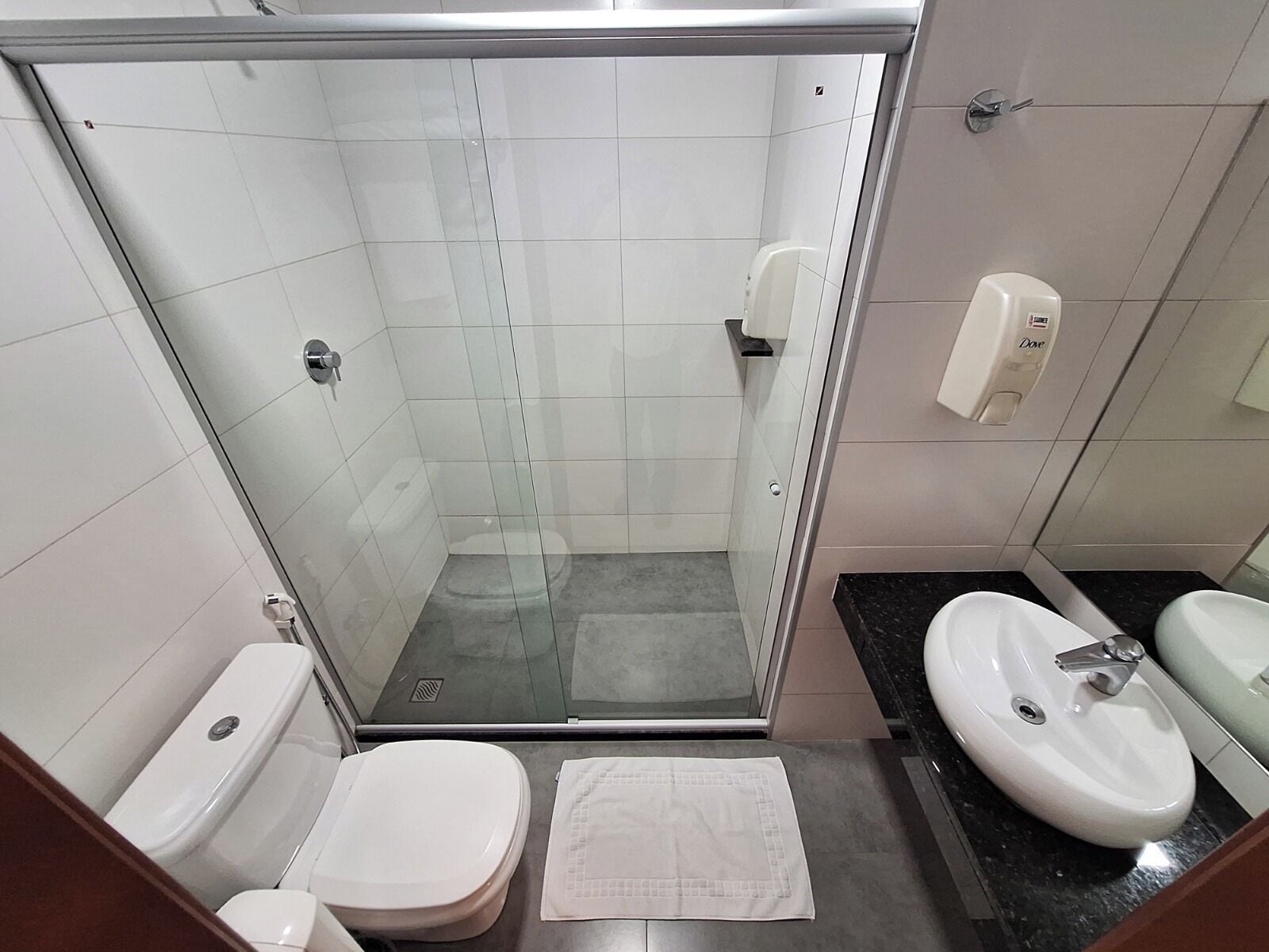 Casa de banho moderna com cabine de hidromassagem em vidro, sanita, lavatório e secador de mãos.