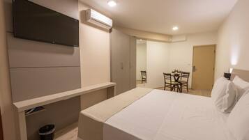 Une chambre d’hôtel avec un lit, un téléviseur fixé au mur, une petite table avec des chaises et une porte donnant sur une autre pièce.