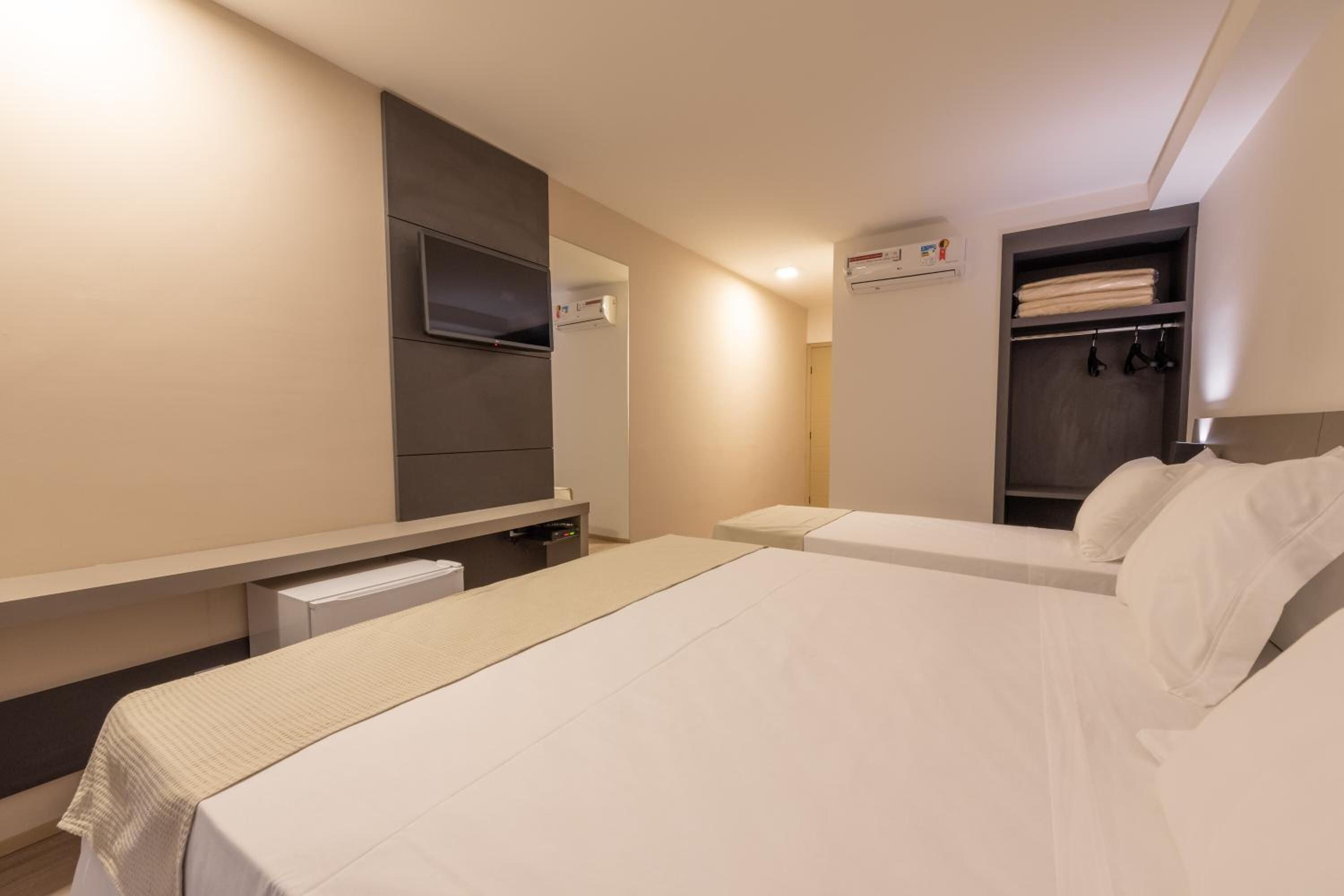 A hotel room with a bed, a TV mounted on the wall, a wardrobe, and a small desk with a chair.