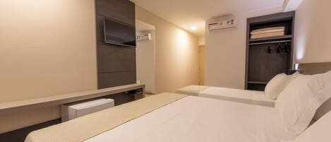 A hotel room with a bed, a TV mounted on the wall, a wardrobe, and a small desk with a chair.