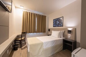 A hotel room with a bed, a desk, a chair, a small table, a trash bin, and a picture on the wall. - Via Garden Varginha Hotel (Varginha)
