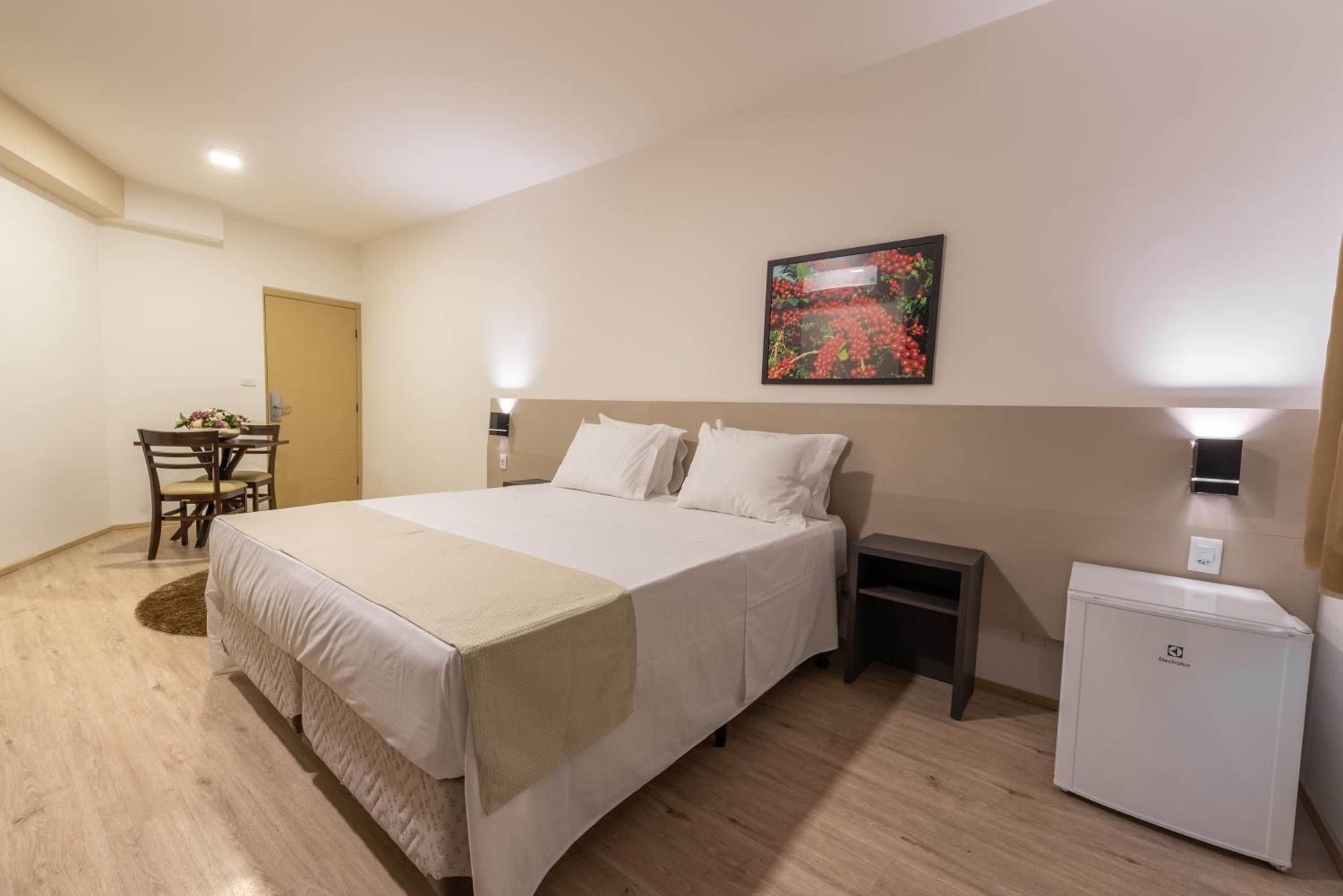 Una habitación de hotel con una cama, mesitas de noche, un escritorio con silla y un refrigerador.