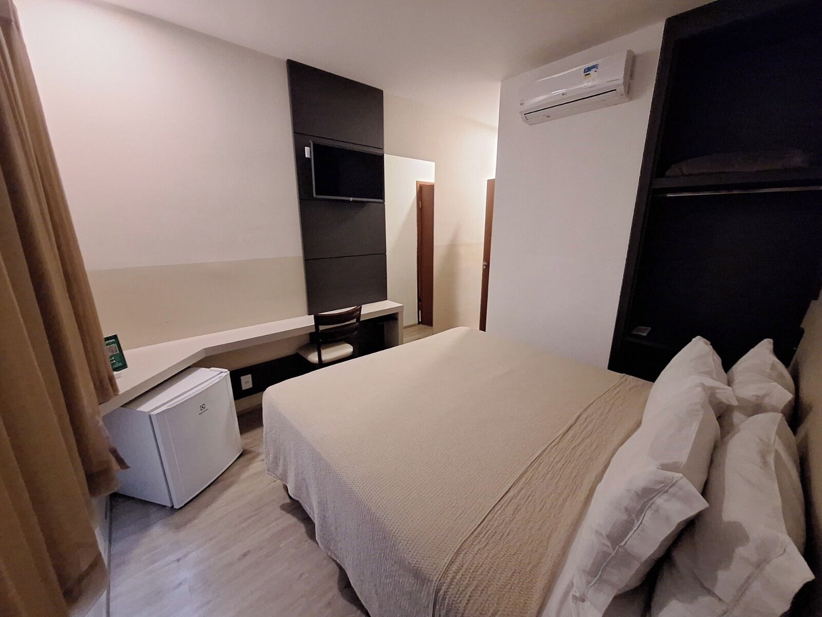 A hotel room with a bed, a small desk, a television, and an air conditioning unit.