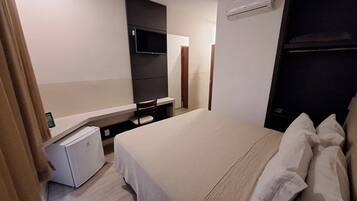 A hotel room with a bed, a small desk, a television, and an air conditioning unit.