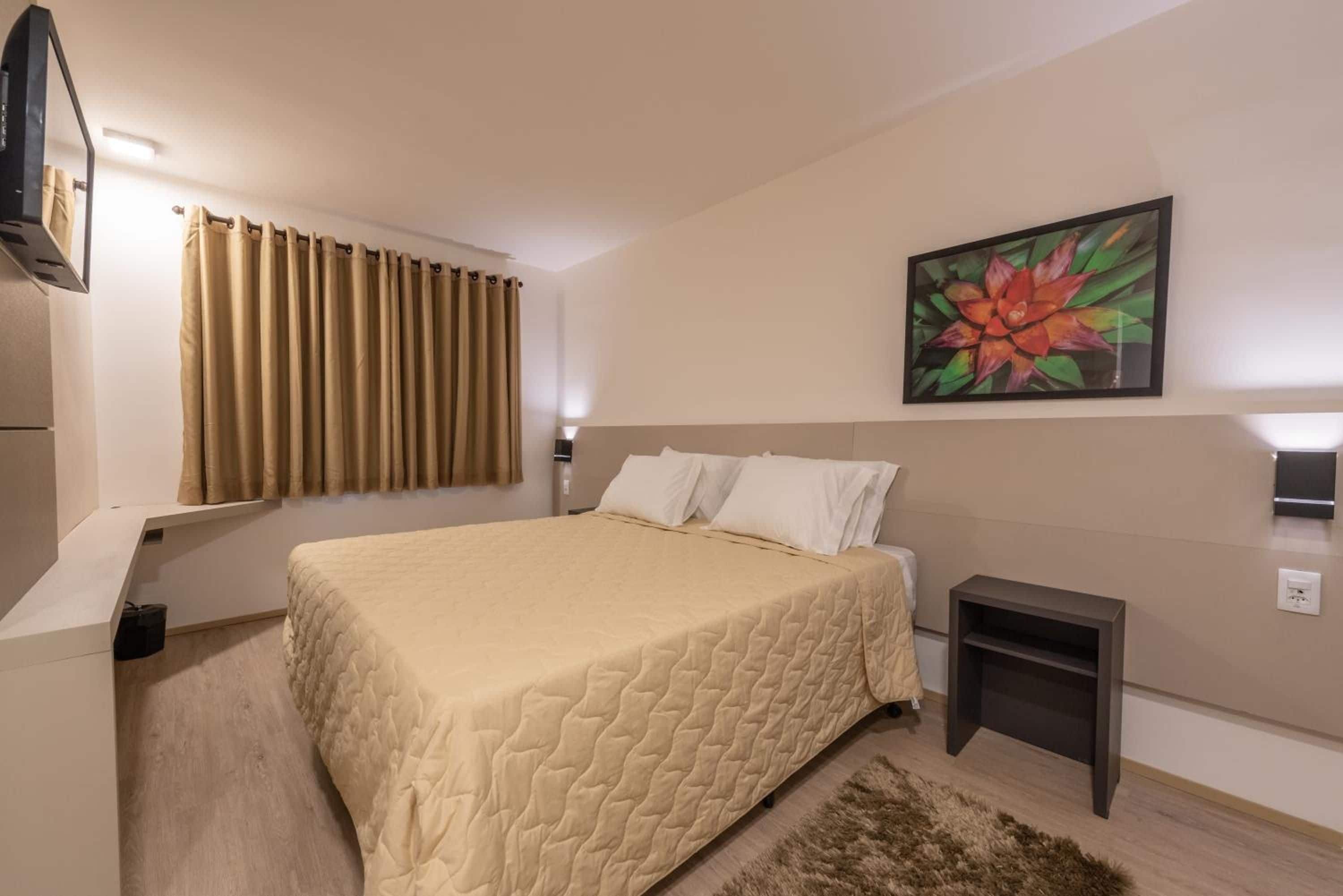Ein Hotelzimmer mit einem Bett, einem Nachttisch, einem Gemälde und einem Fenster mit Vorhängen.