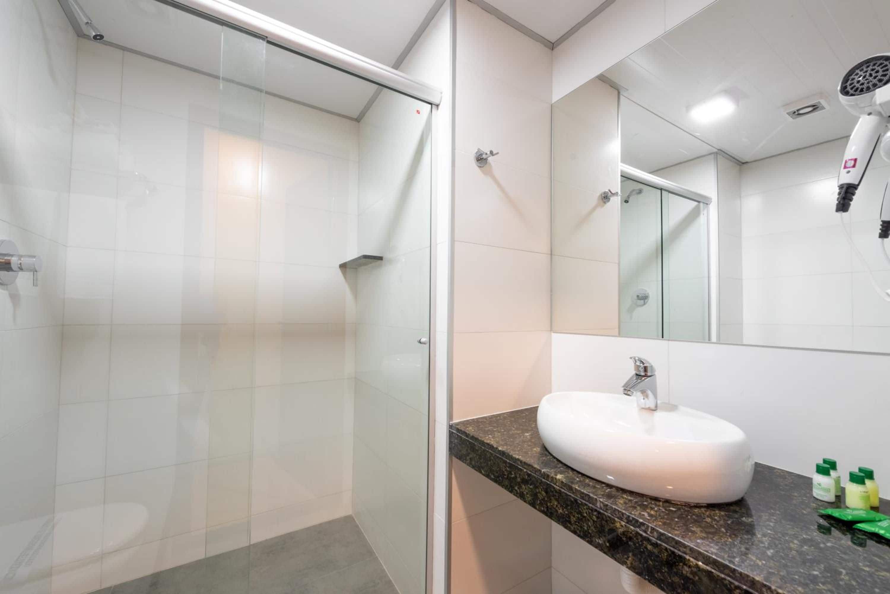 Un baño moderno con cabina de ducha de vidrio, un lavabo blanco y un espejo grande.