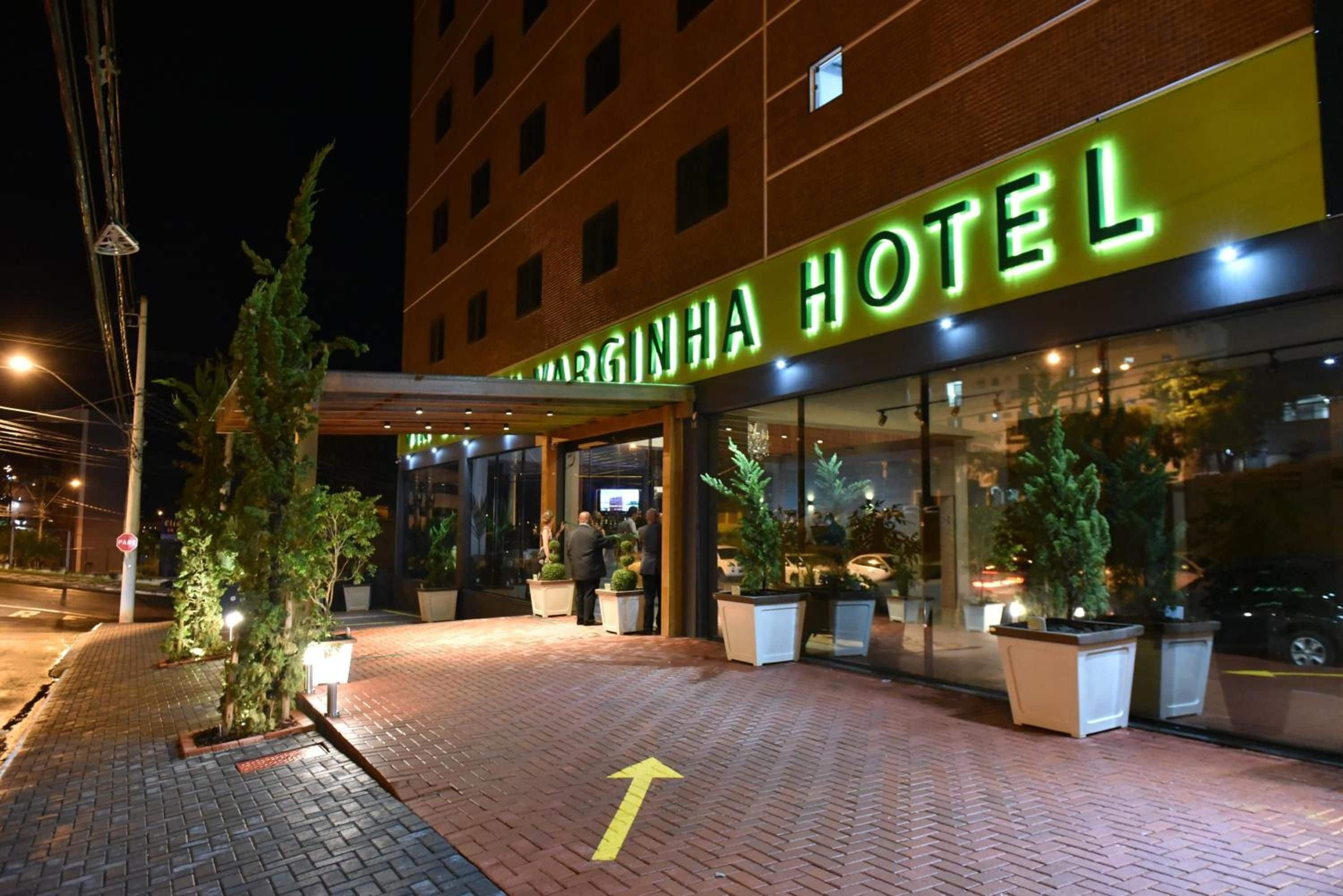 Entrada de hotel con un camino despejado señalizado por una flecha, plantas en macetas y una fachada bien iluminada.