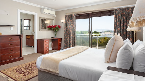 Ein Hotelzimmer mit einem großen Bett, einem Schreibtisch, einer Kommode, einem Spiegel und Blick ins Freie.
