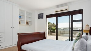 Ein Schlafzimmer mit einem hölzernen Bett, weißer Bettwäsche, einem weißen Kleiderschrank und Blick durch ein großes Fenster.