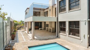 Ein modernes, zweistöckiges Haus mit Glasbalkon, Swimmingpool und Terrassenbereich.