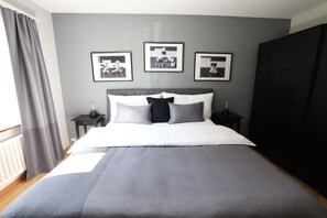 A bedroom with a bed, grey curtains, a radiator, and framed pictures on the wall.
