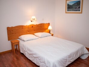 Ein ordentlich bezogenes Bett mit weißer Bettwäsche und Kissen, ein Holz-Kopfbrett und ein kleiner Nachttisch mit einer Lampe.