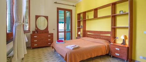 A bedroom with a bed, a dresser, a mirror, and a shelf unit.