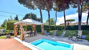 Um quintal com piscina, área de estar coberta e móveis de exterior.