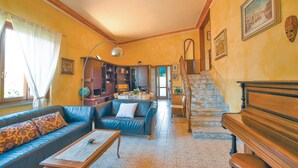 Uma sala de estar com sofá, mesa de centro e um piano. Escada leva a outro ambiente.