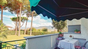 Um terraço com mesa e cadeiras, um vaso de planta e vista para árvores e casas.