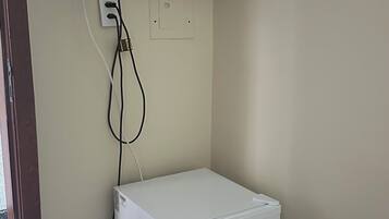 A white refrigerator with a '10 ANOS' sticker, a flat-screen TV mounted above it, and a power outlet on the wall.