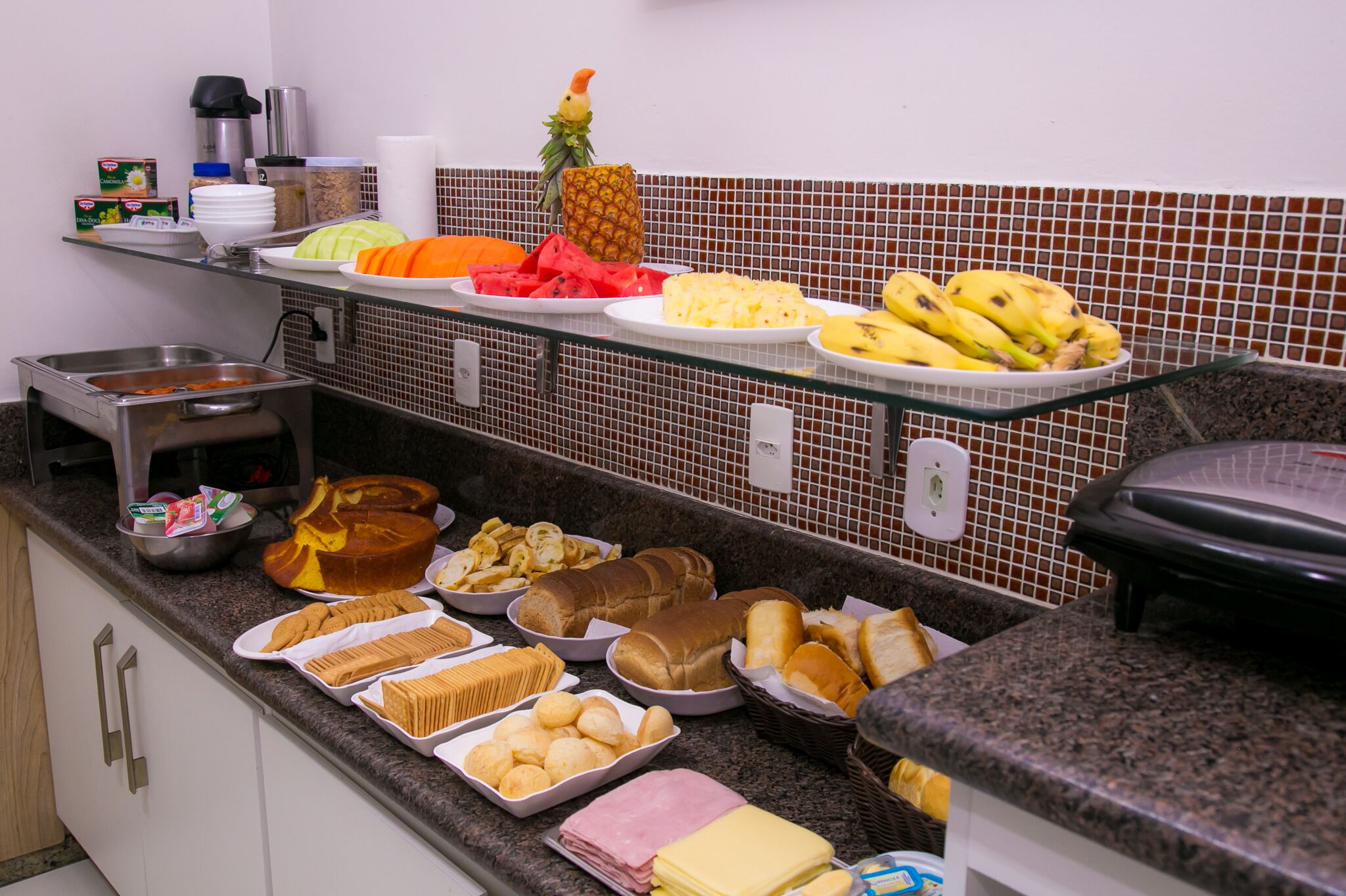 A buffet with various food items including fruits, bread, and pastries.