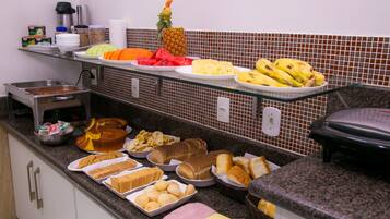 A buffet with various food items including fruits, bread, and pastries.