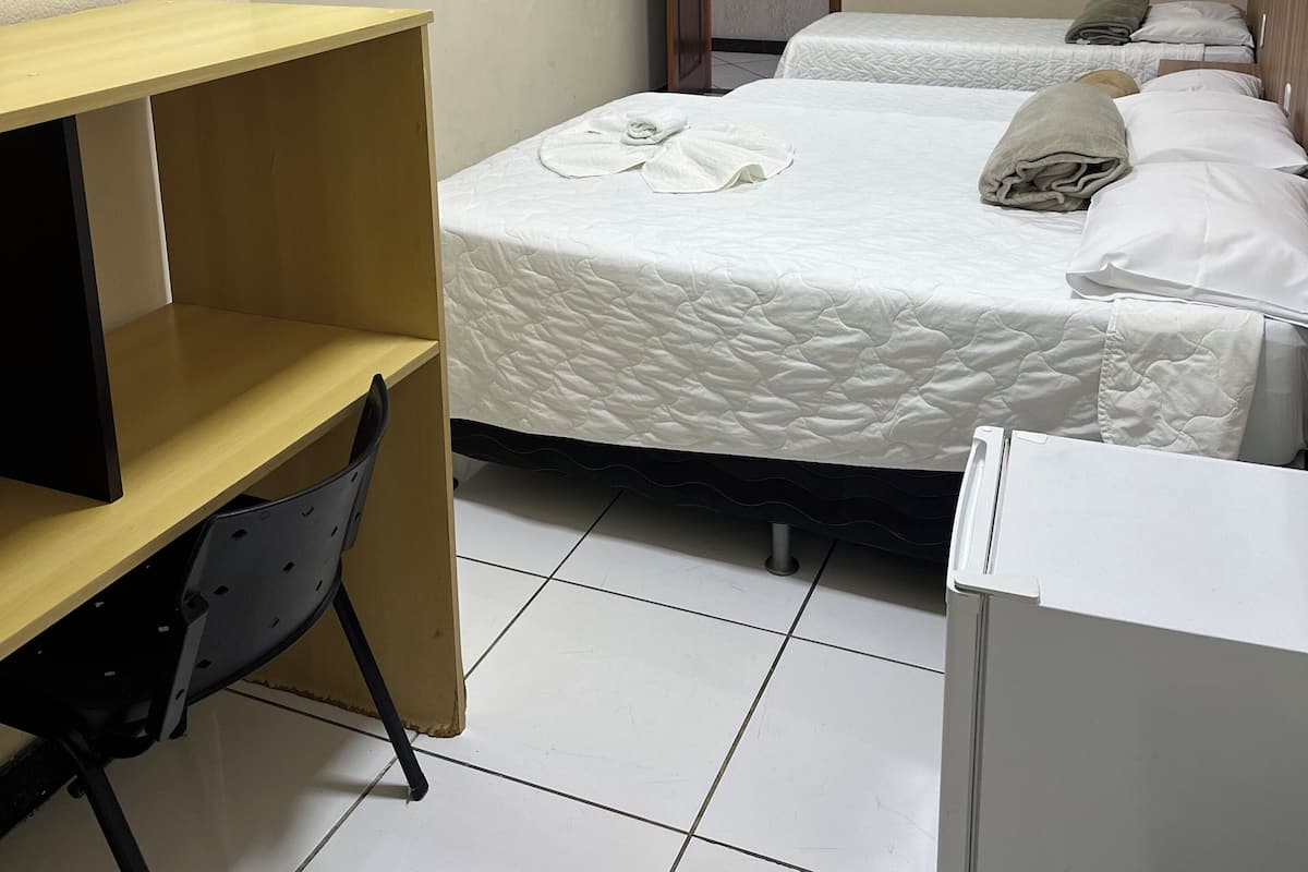 A hotel room with two beds, a desk, a chair, a television, and a door.