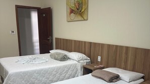 A hotel room with two single beds, a wooden headboard, a painting on the wall, and a door. - GV Park Hotel (Governador Valadares)