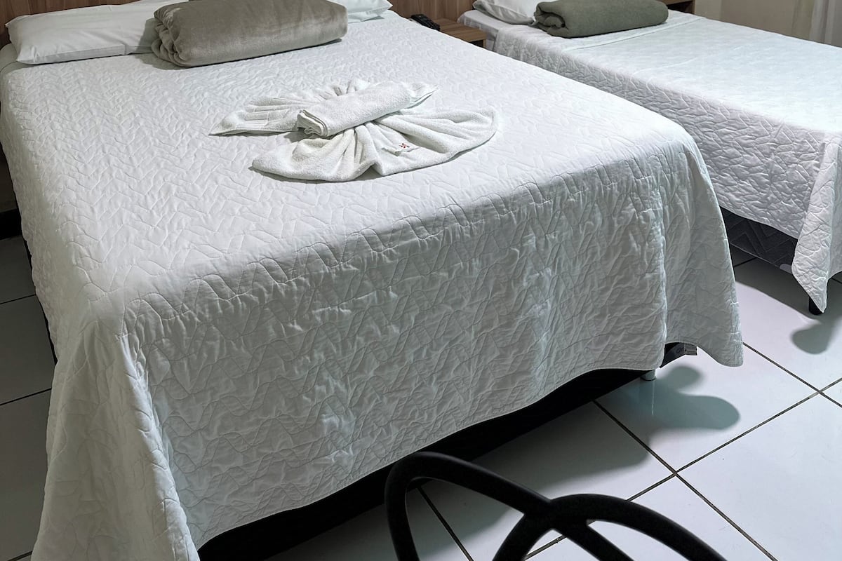 Two single beds with white linens and a wooden headboard, a small bedside table, and a tiled floor.